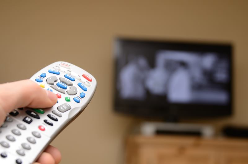 Hand holding remote aiming toward a TV currently playing a television program