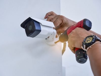 A CCTV camera being installed on a wall by a Man using a red drill.