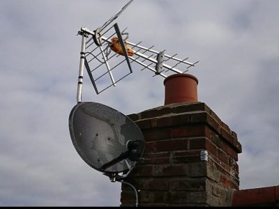 An aerial and satellite attached to the chimney of a house